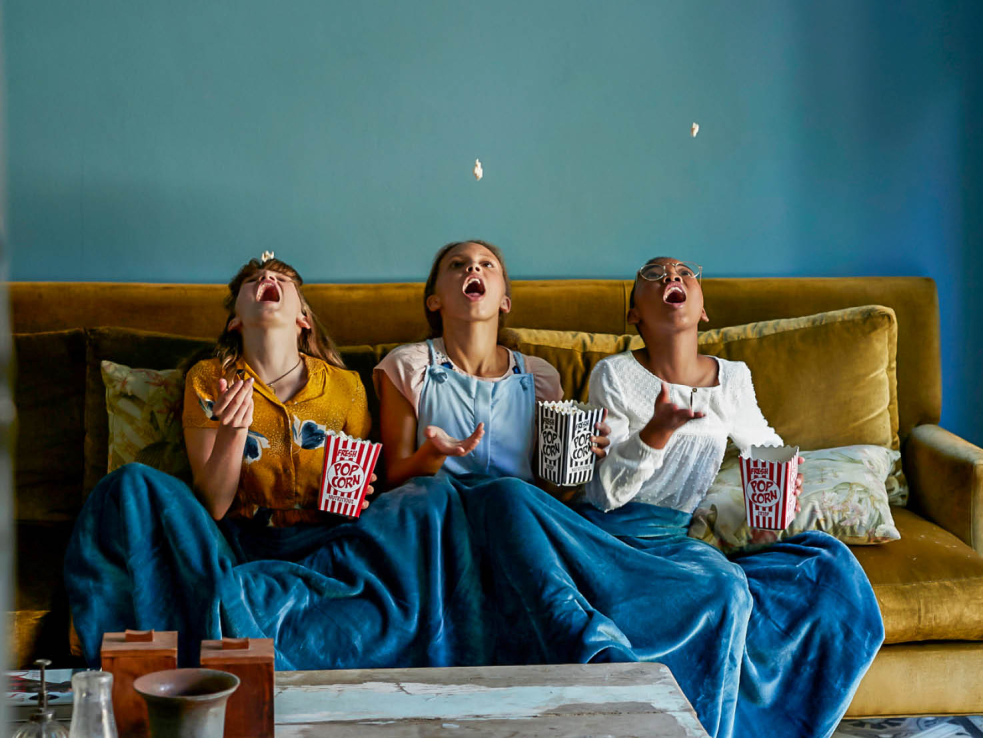 Drei Kinder auf einem Sofa geniessen Popcorn.